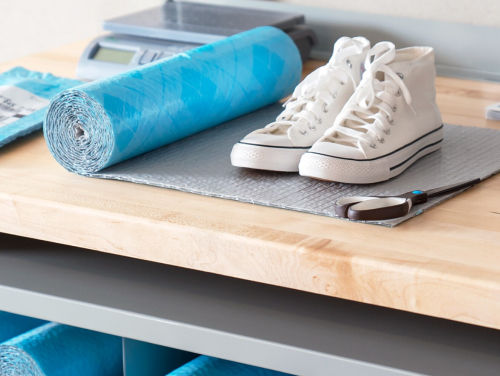 A pair of white high-top sneakers placed on a wooden workbench next to a rolled-up blue foam mat.