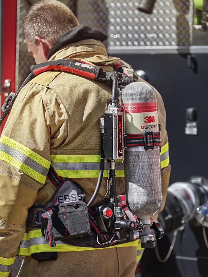 Close-up of a firefighter wearing turnout gear and a SCOTT 3M self-contained breathing apparatus (SCBA) air tank on their back.