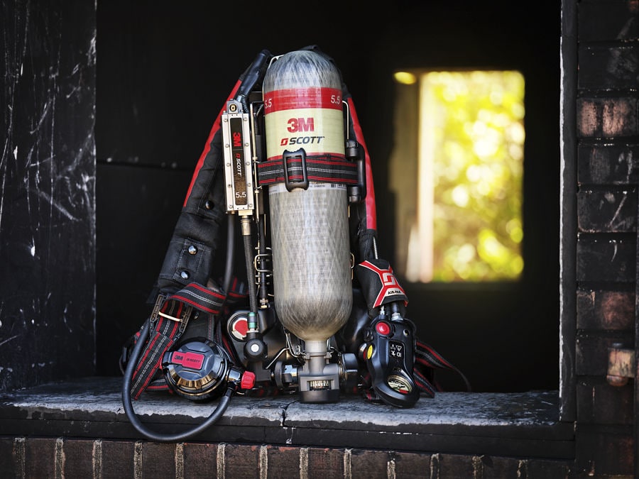 3M Scott SCBA air cylinder and firefighter turnout jacket hanging inside a dark fire station bay.