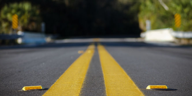 Low angle view down a long straight road, reflective cat's eye road stud placed in standard intervals 