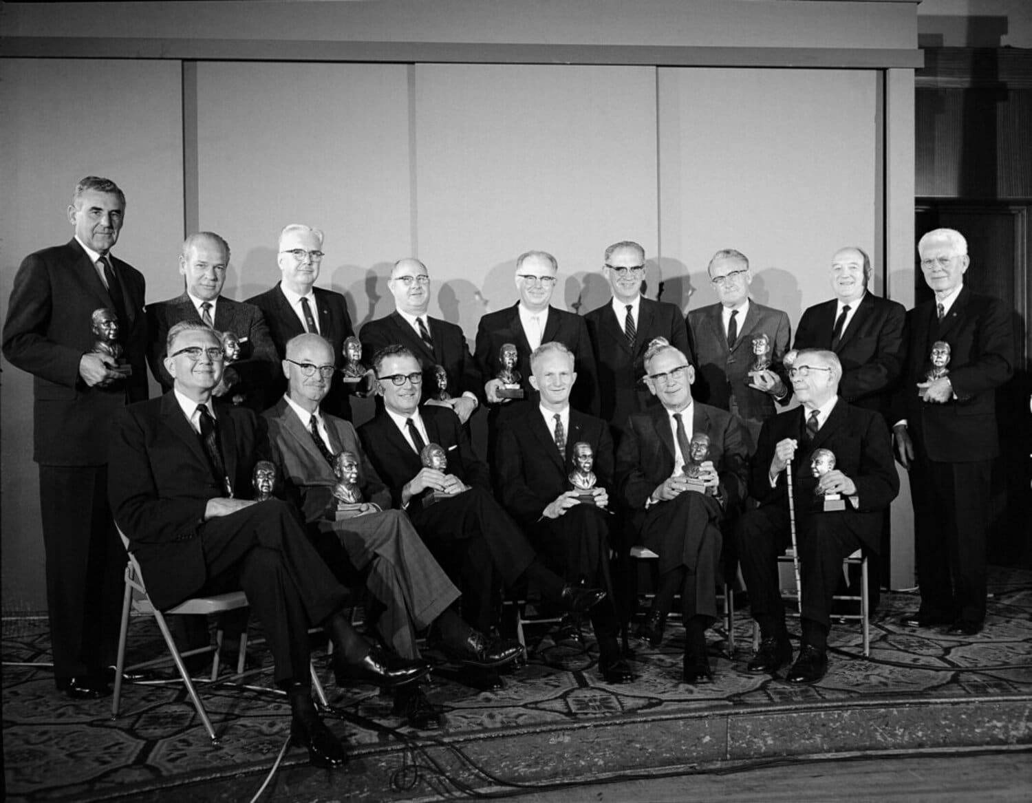 A group of individuals in formal attire is holding awards, with text on the left side reading: The Carlton Society. 