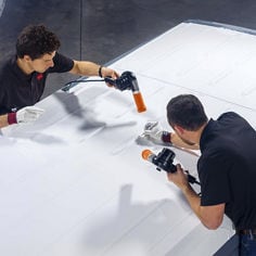 Two men hold heat guns close to cooling film as they apply it to a vehicle roof.