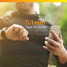 Lifestyle image of a person holding a phone with thickness callout for the tape. 0.1 mm tape thickness.