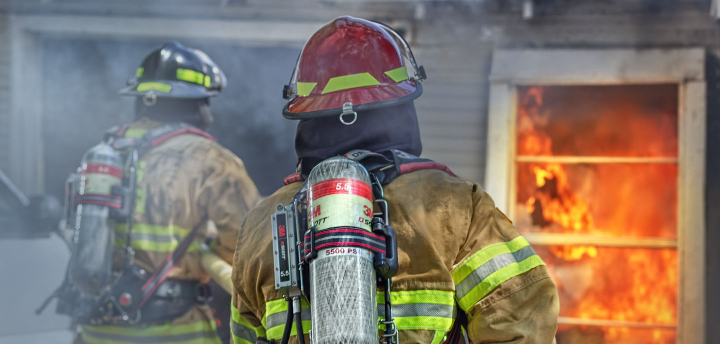 Firefighters facing a burning house with Scott Safety equipment on 
