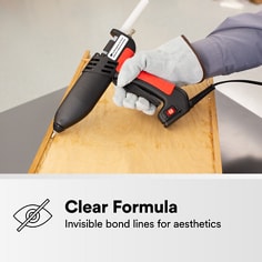Hot melt applicator applies clear adhesive to a wood surface. The asset states Clear Formula, invisible bond lines for aesthetics.