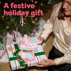 Post-it® brand holiday lifestyle scene with gifts and notes on a table near a Christmas tree. Text reads "A festive holiday gift."