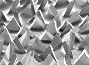 A pattern of triangular, pyramid-like structures arranged in rows, creating a textured surface with varying shades of gray.