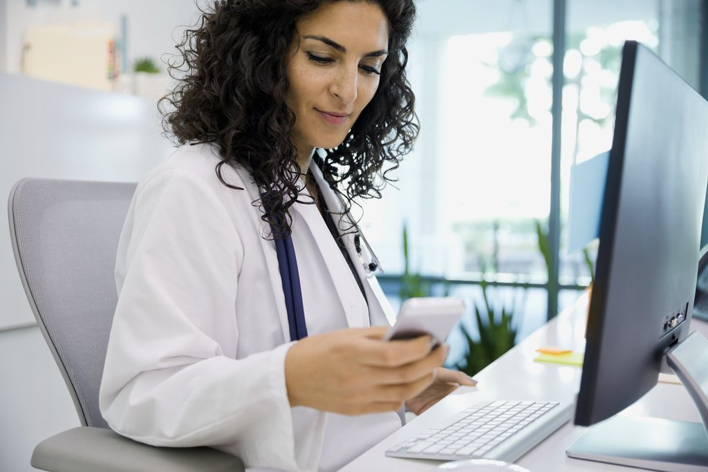 Doctor sitting by her computer while on her phone. 