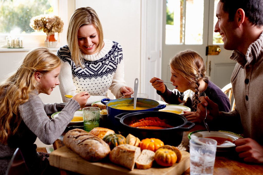 Une famille qui mange et qui sourit assise autour d’une table.